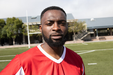 African American man standing on artificial turf field wearing red and white jersey near goalpost