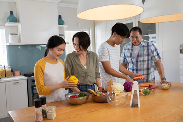 Asian family chopping bell peppers, mixing salad at kitchen island under pendant lights