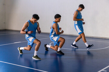 African american male teammates doing front lunges on basketball court in blue jerseys, sneakers