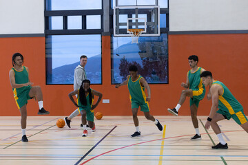 Basketball coach along with five players in green jerseys performing lunges under hoop