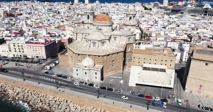 Aerial drone cityscape view of Cadiz in Spain, Andalusia, Europe, on bright sunny day, facing C&aacute;diz Cathedral and waterfront. Drone rising slowly with camera tilting down. Cinematic dark grading