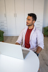 Fototapeta premium Man sitting in home office at white round table with laptop near cabinets, copy space