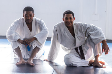 African american training partners sitting on mats in martial arts gym in white gis and belts