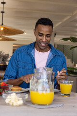 African american man sitting at table in cafe area and cutting pancakes beside glass of juice