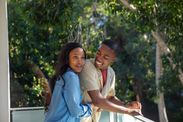 African American couple standing on balcony leaning against glass railing sharing tender glance