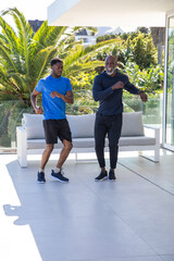 African american father and son dancing on patio by sofa, tropical plants, wearing sneakers © wavebreak3