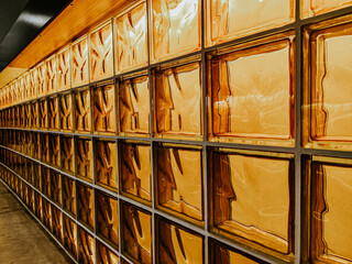 Textured glass block wall with amber tones and reflections creates a warm atmosphere in a modern interior space, enhancing the aesthetic appeal of the environment
