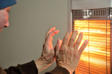 電気ストーブで暖をとる老人