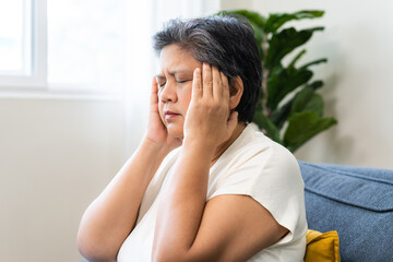 Unhappy asian elderly woman sitting on sofa at home, sick and stress headache feeling depressed suffering trauma from problem trouble tension, old tired difficulty mental health, senior exhausted pain