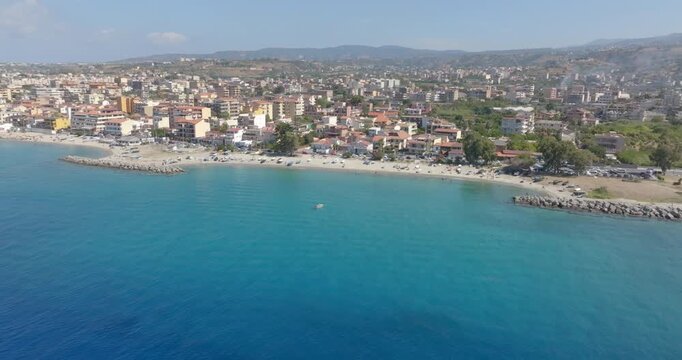 High-angle aerial view of a sandy beach adjacent to a coastal village. Turquoise waters create a picturesque and authentic Mediterranean scene. It is Gallico Beach, in Calabria, southern Italy.
