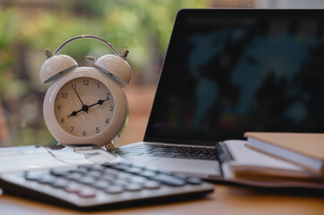 Alarm clock with laptop, calculator and notebook on desk representing time management,...