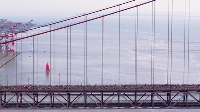 Side-on aerial drone shot of half marathon and 10K long-distance running event in Lisbon, Portugal, Europe. Runners crossing the iconic famous red 25th April suspension bridge. Commercial grading