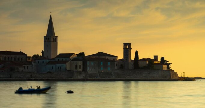 Porec, Croatia - August 13, 2025: Timelapse. Scenic sunset view of Porec old town skyline with Euphrasian Basilica tower and blurred boat on calm Adriatic Sea in Croatia