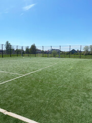 Green artificial turf sports field with goalposts and surrounding fence under a clear blue sky, ideal for mini-football or handball activities with ample space for play