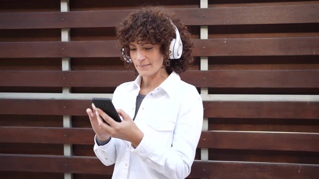 A Young Woman is Happily Enjoying Music on Her Smartphone While Wearing Headphones