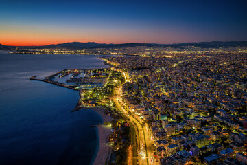 Aerial view of the illuminated skyline of Athens, Greece, with the southern coastal road next to beaches and marinas during dusk