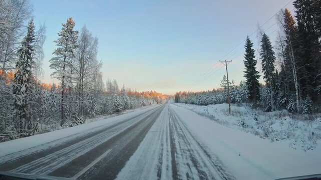 Front window point of view driving on snow covered winter road in Lapland with frozen forest sunrise light icy asphalt and Nordic countryside winter travel atmosphere