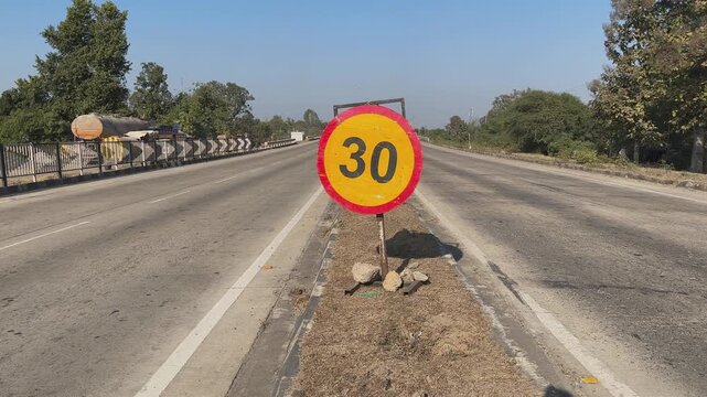Tracking shot of a temporary speed limit 30 sign swaying slightly from wind and passing vehicles, work zone visible ahead under clear sky