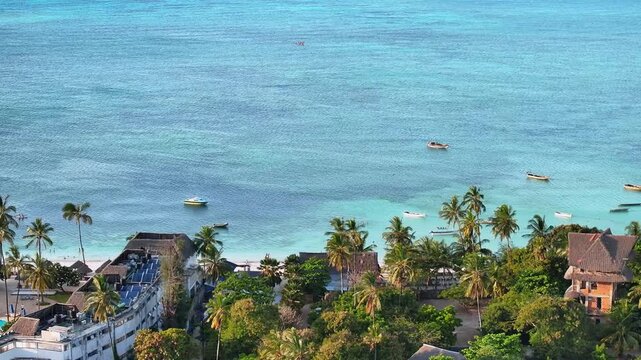 Cinematic drone 3x zoom shot flying along tropical beach resorts and the ocean in Zanzibar. Detailed coastline, turquoise water, and luxury seaside atmosphere create a stunning travel and vacation sce