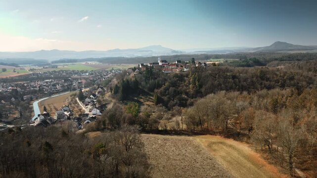 Dynamic forward drone flight approaches Aach village perched on hills with river, dense autumn woods, fields, and distant mountains under clear skies. Perfect for travel docs, regional ads