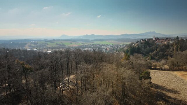 Smooth downward drone descent reveals Aach village amid autumn forests, fields, and rugged hills under partly cloudy skies. Perfect for travel docs, regional ads, cinematic reveals.
