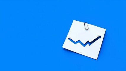 White paper note with cut-out upward trending arrow graph attached by a black paperclip on a vibrant blue background, representing financial growth.