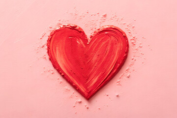 A vibrant red heart shape created from cosmetic pigment on a soft pink background