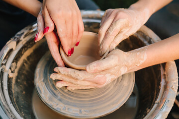 Teaching of shaping clay into a smooth ceramic vessel with precision. Two pairs of hands work together on the pottery wheel, shaping clay into form.