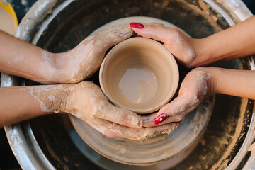 Teaching of shaping clay into a smooth ceramic vessel with precision. Two pairs of hands work...