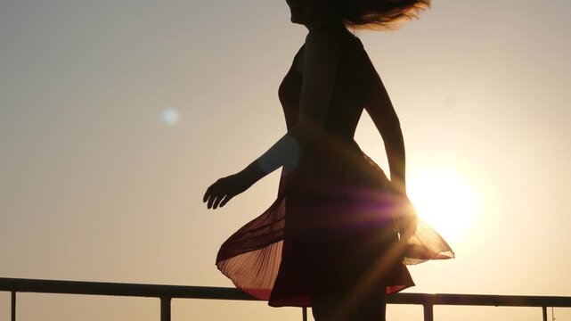 Happy young woman dance in light dress against bright sun, turn around to express positive emotions. Light dress and zephyr skirt fly round, camera tilt up and down. Elegant woman have good moments