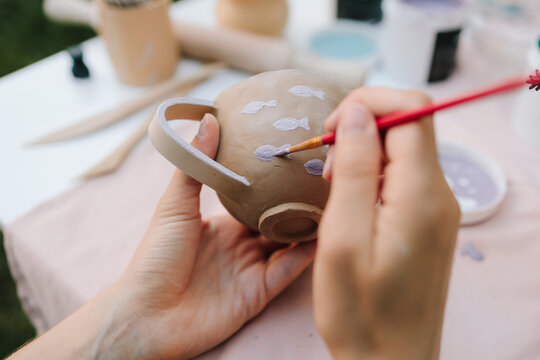 Ceramic painting of mug with fish pattern using brush strokes. Artist paints delicate purple fish on a handmade clay mug. Painting ceramic mug with purple fish using brush and paint.