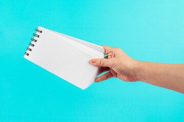 A white notebook in hand against a blue background.