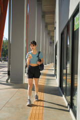 Young Asian woman walking after workout while checking smartphone outside gym building