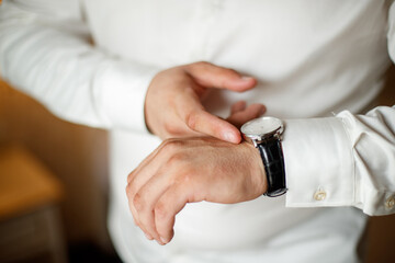 A man in a suit is wearing a watch and adjusting his jacket. The image has a blurry quality, which gives it a sense of motion and action. The man's focus on his watch