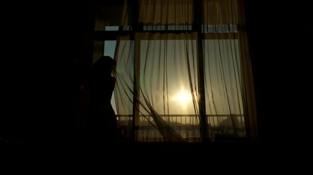 Woman draw transparent curtain and stuck, correct and close window, black silhouetted shot. Bright morning sun shine on clear sky, Girl slide light zephyr drape over large glass