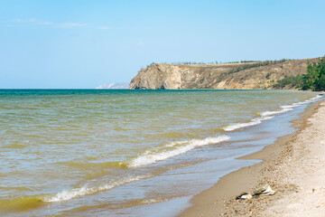 Rocky shore of Olkhon island on Baikal lake with sandy beach and wave. Concept of travel, nature, Siberia, Russia, vacation.