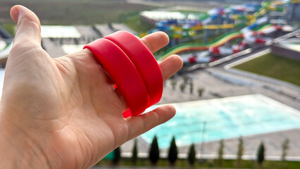 Vibrant red wristbands clench adventure in Caucasian female hand, poised for splashy escapades at a vivid water park, invoking World Water Day zeal