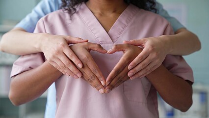 Diverse medical professionals wearing scrubs forming a heart shape with their hands as a symbol of unity and patient care in a clinic