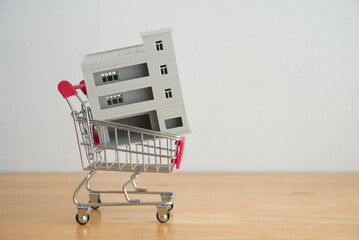 Commercial building in shopping trolley on wooden table with white wall background copy space. Commercial real estate investment, real estate investment trust (REIT), entrepreneur, business concept.