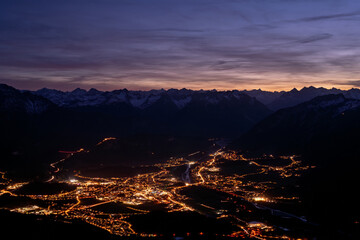 Night view of the town of Reutte in the Außerfern region of Tyrol, seen from Mount Säuling in the Allgäu Alps, Austria, illuminated valley lights beneath a dark alpine sky. © ikoon