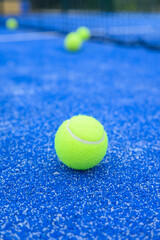 Padel court detail with several neon green balls on the textured blue surface.