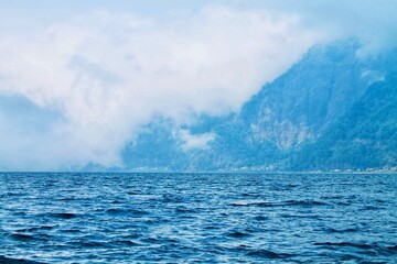 Scenic view of Mount Batur from Lake Batur in Bali, Indonesia. Wide composition, calm water surface, misty volcanic mountains. Perfect for travel, nature, background, wellness themes. © Arlina Elsiska