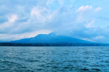 Scenic view of Mount Batur from Lake Batur in Bali, Indonesia. Wide composition, calm water surface, misty volcanic mountains. Perfect for travel, nature, background, wellness themes. © Arlina Elsiska