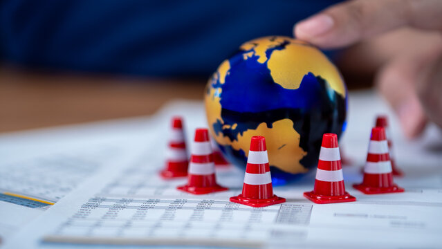 Global risk management and crisis warning for the world economy. This safety concept uses a globe surrounded by traffic cones on financial documents to geopolitical boundaries and trade barriers.
