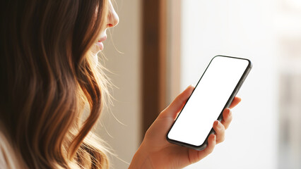 Hand holding mobile phone with blank white mockup screen by woman in warm minimalist home office interior, professional digital device for creative app and brand showcase presentation.
