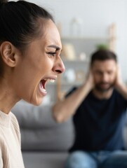 A woman is screaming in frustration while a man covers his ears, showing distress. Tension and conflict in relationships.