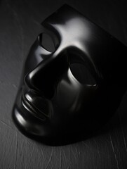 A black theatrical mask positioned on a dark textured surface. Symbol of mystery and performance art.