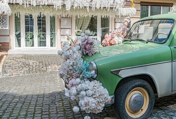 A vintage green car with a yellow roof, parked on a cobblestone street in an urban European setting...