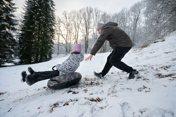 Man pushes a sled with a woman on a snowy hill in winter.