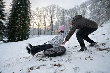 Man pushes a sled with a woman on a snowy hill in winter.